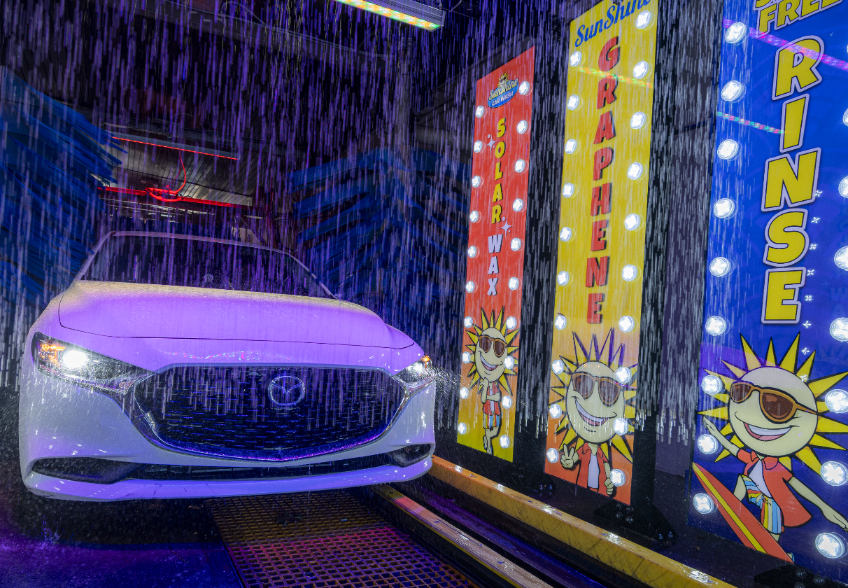 A car getting rinsed inside the Sunshine wash tunnel beneath colorful Solar Wax, Graphene and Rinse signs