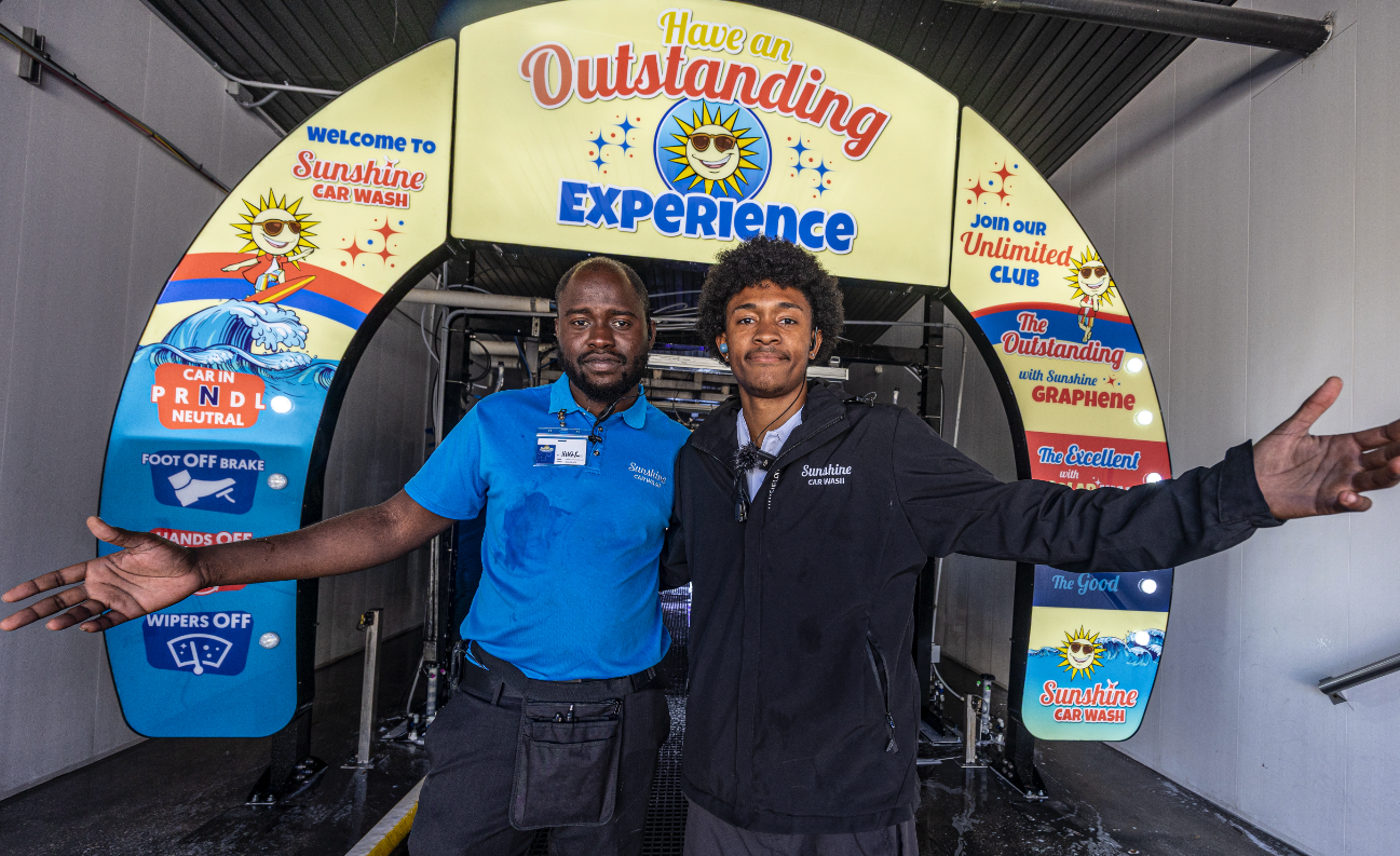 Two Sunshine team members welcoming guests beneath the Have an Outstanding Experience tunnel arch