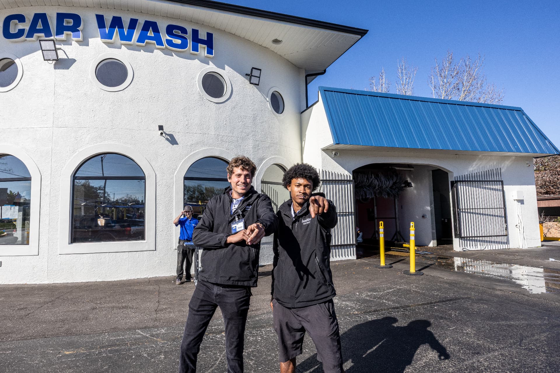 Two smiling Sunshine team members pointing the way in front of the Fowler Avenue building