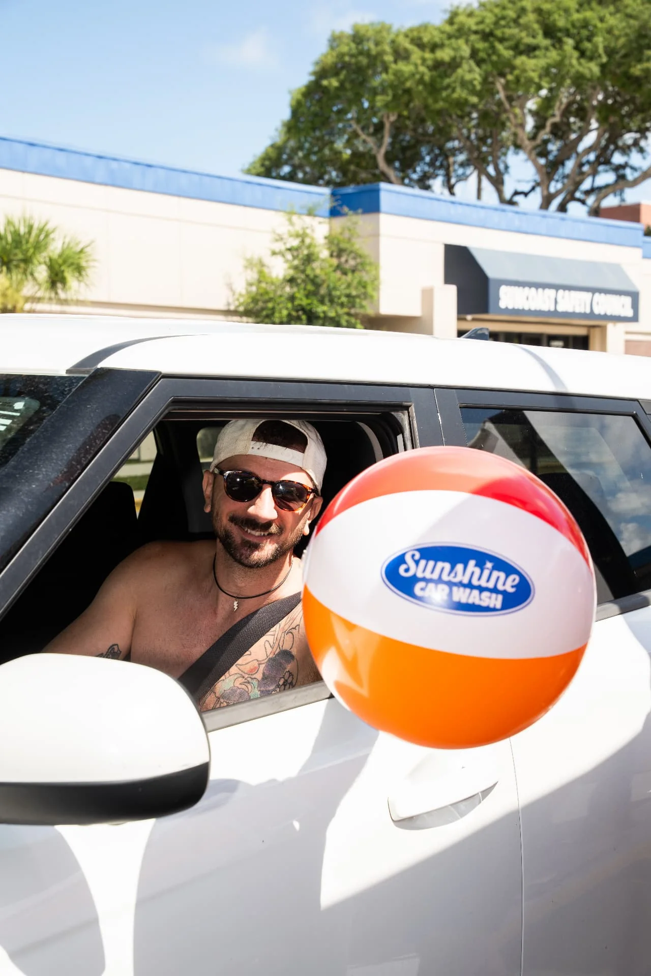A happy Sunshine customer holding a Sunshine Car Wash beach ball out of his car window