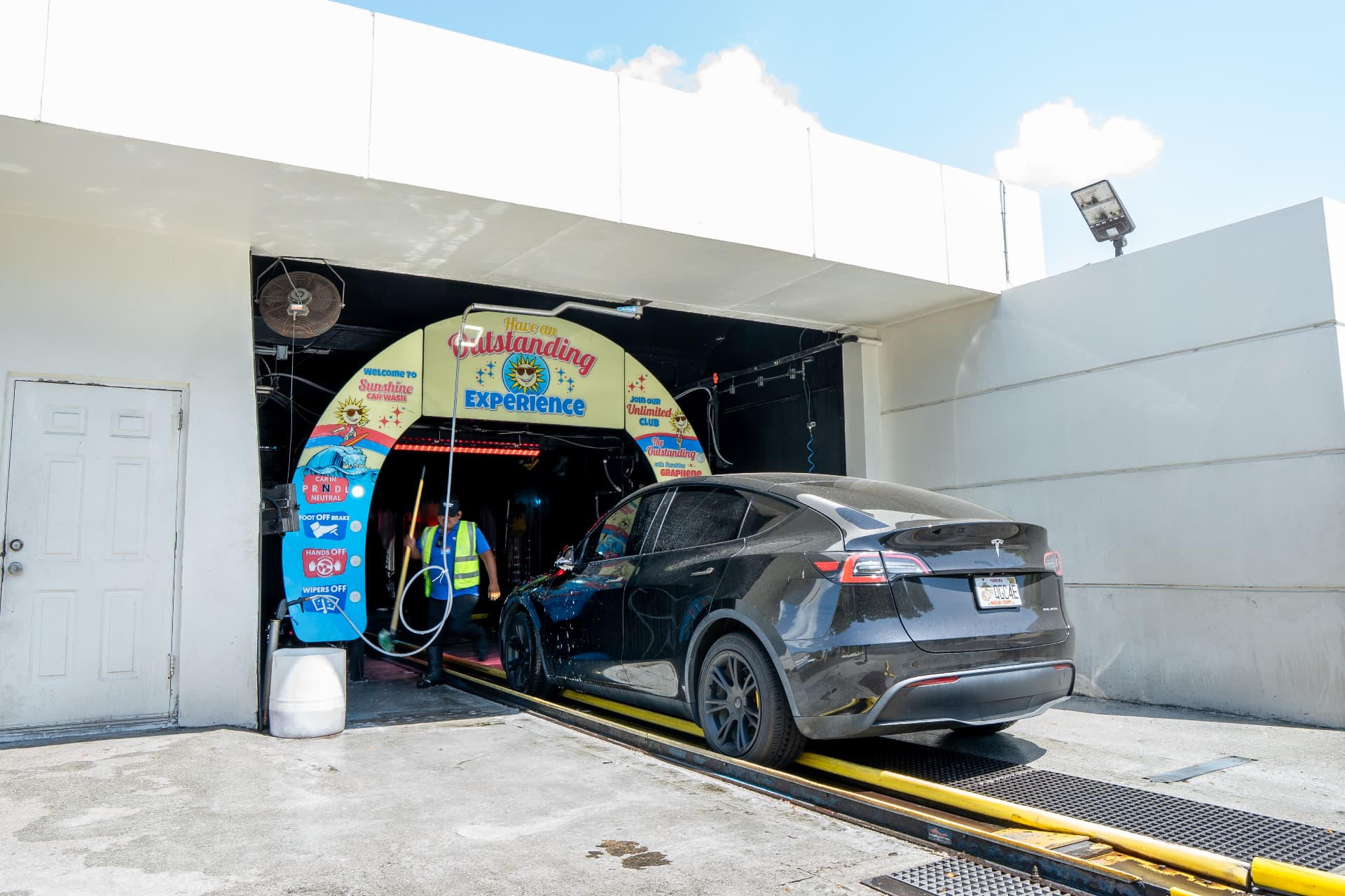 A black SUV entering the wash tunnel beneath the Have an Outstanding Experience arch
